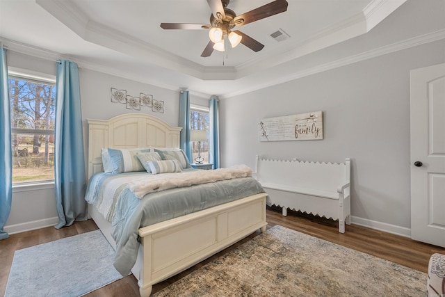 bedroom featuring a raised ceiling, multiple windows, wood finished floors, and visible vents