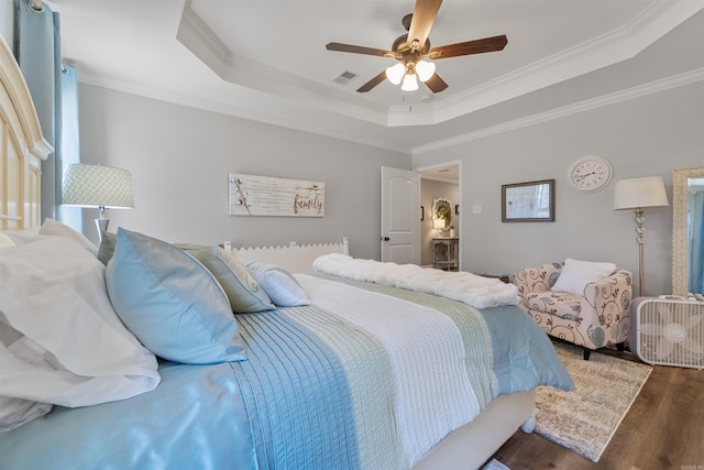 bedroom featuring a tray ceiling, visible vents, wood finished floors, and crown molding