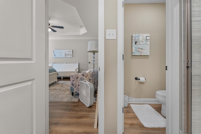 bathroom featuring crown molding, ceiling fan, toilet, a tray ceiling, and wood finished floors