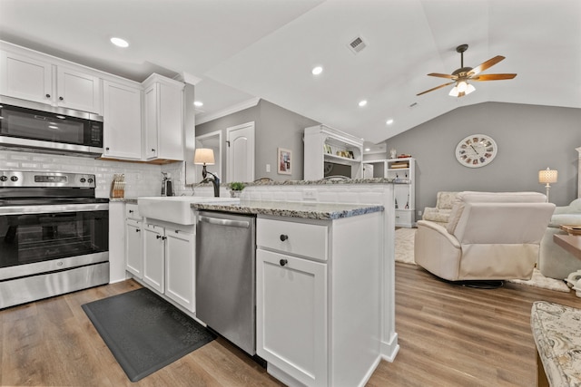 kitchen featuring visible vents, a peninsula, a sink, appliances with stainless steel finishes, and open floor plan