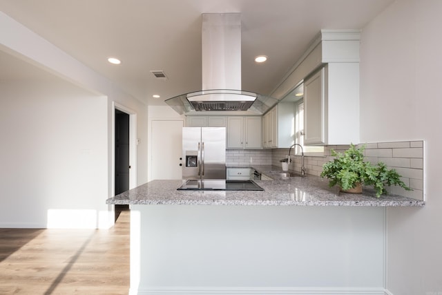 kitchen with black electric stovetop, light stone countertops, stainless steel fridge with ice dispenser, island range hood, and a sink