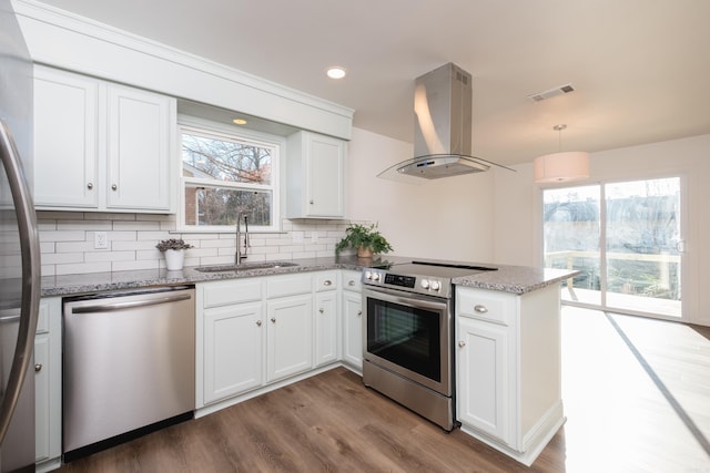 kitchen featuring visible vents, a sink, a peninsula, appliances with stainless steel finishes, and wall chimney exhaust hood