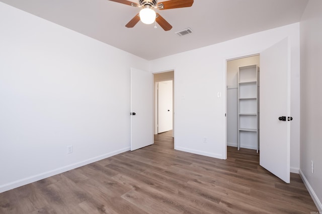 unfurnished bedroom featuring visible vents, a walk in closet, baseboards, wood finished floors, and a closet