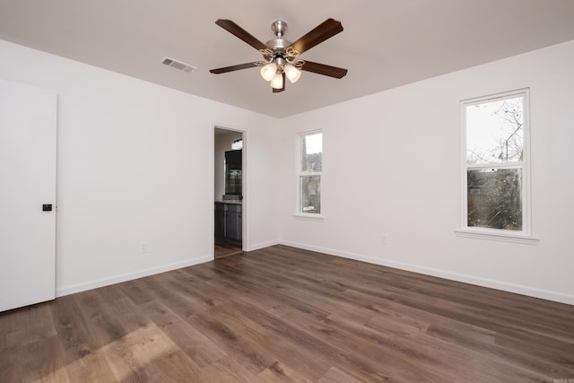 empty room featuring dark wood-style floors, visible vents, a ceiling fan, and baseboards