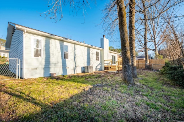 back of property with a lawn, fence, crawl space, central AC unit, and a chimney