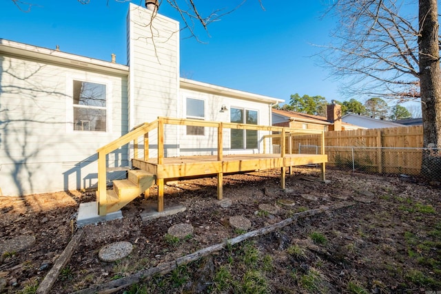 rear view of house featuring a wooden deck, a chimney, and fence