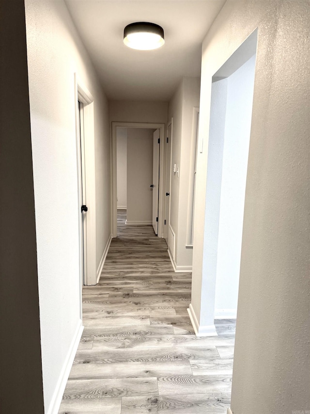 corridor with baseboards and light wood finished floors