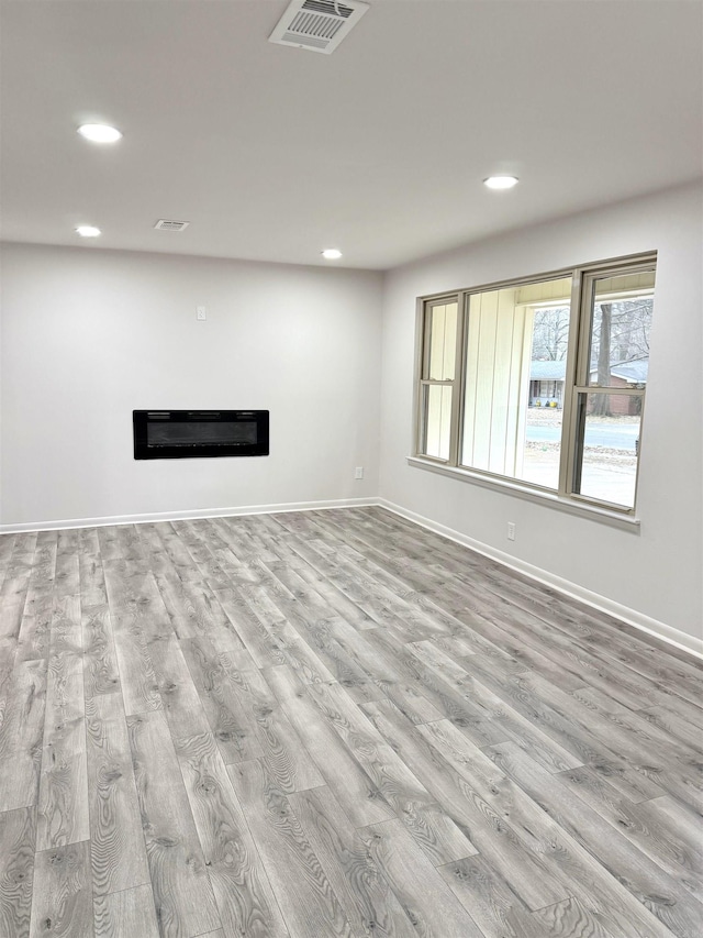 unfurnished living room featuring wood finished floors, visible vents, baseboards, recessed lighting, and a glass covered fireplace