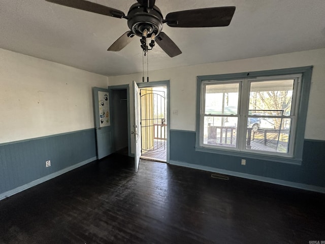 empty room with a wainscoted wall, baseboards, dark wood-type flooring, and visible vents