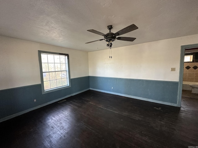 spare room featuring wood finished floors, visible vents, wainscoting, ceiling fan, and a textured ceiling