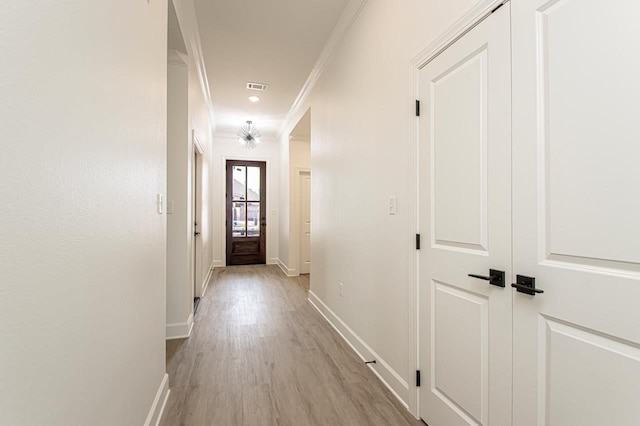 hall featuring light wood finished floors, visible vents, baseboards, and ornamental molding