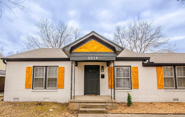 view of front facade featuring brick siding, roof with shingles, and crawl space