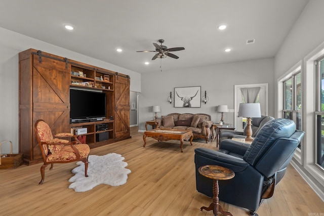 living room featuring a barn door, recessed lighting, light wood-style floors, and visible vents