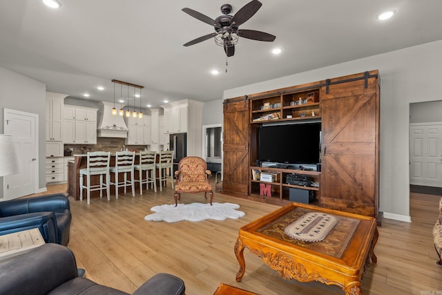 living area with baseboards, a barn door, recessed lighting, light wood-style flooring, and a ceiling fan