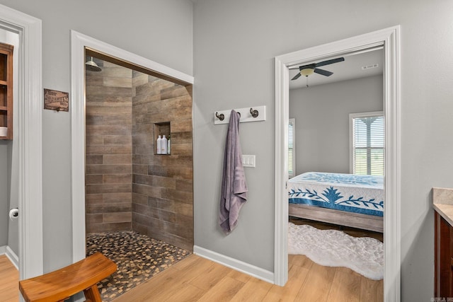 bathroom with ensuite bathroom, wood finished floors, tiled shower, baseboards, and ceiling fan