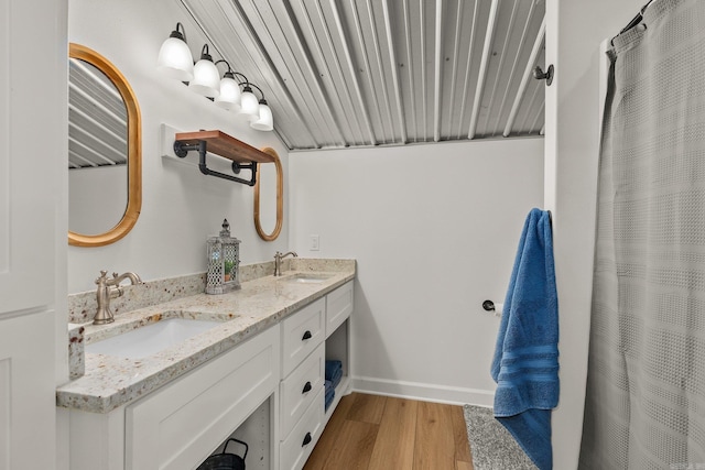 full bathroom featuring a sink, baseboards, wood finished floors, and double vanity