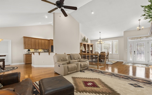 living area featuring ceiling fan with notable chandelier, high vaulted ceiling, light wood-type flooring, and baseboards