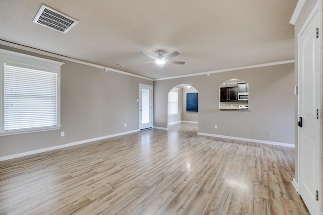 unfurnished living room featuring a ceiling fan, visible vents, light wood-style flooring, arched walkways, and crown molding