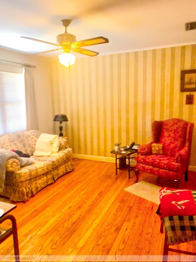 living room with wallpapered walls, wood finished floors, visible vents, and baseboards