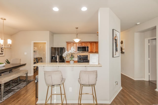 kitchen with washer and clothes dryer, a breakfast bar area, brown cabinets, wood finished floors, and black appliances