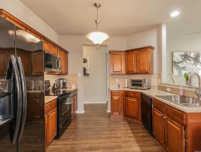 kitchen featuring brown cabinetry, dark wood finished floors, a sink, black appliances, and light countertops