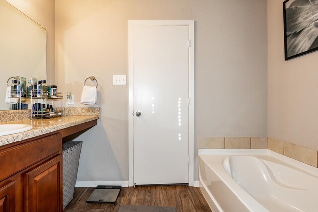 bathroom with vanity, a garden tub, wood finished floors, and baseboards