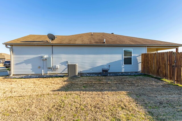 rear view of house featuring a lawn, central AC unit, and fence