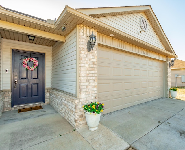 property entrance with a garage, brick siding, and driveway