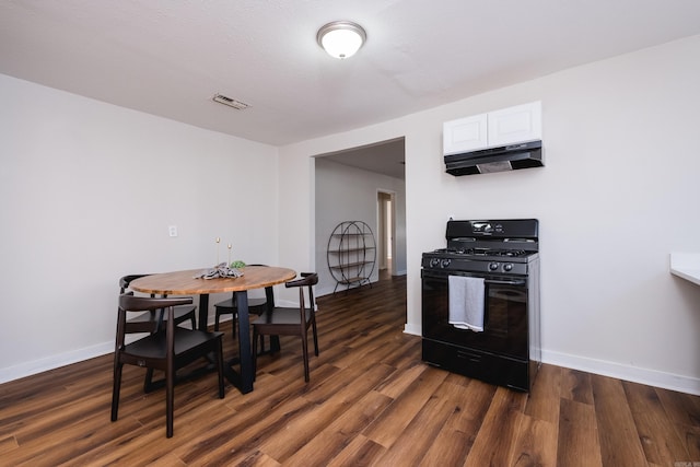 kitchen featuring dark wood-style flooring, gas stove, visible vents, and under cabinet range hood