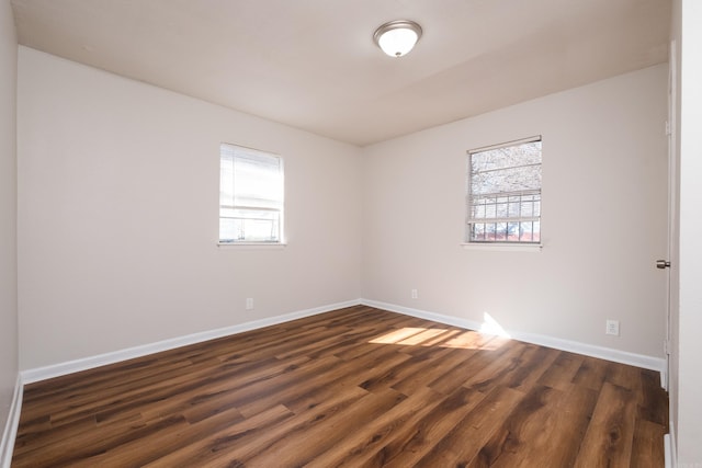 spare room with a wealth of natural light, dark wood-type flooring, and baseboards