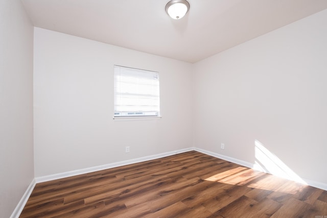 spare room with baseboards and dark wood-style flooring