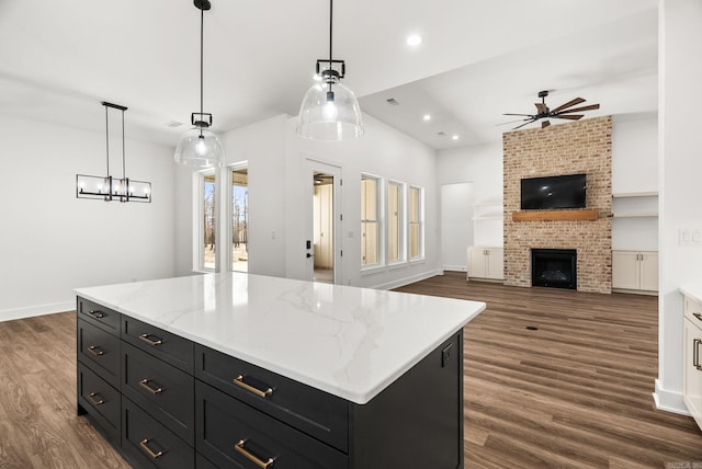 kitchen with dark wood finished floors, a brick fireplace, a ceiling fan, and dark cabinets