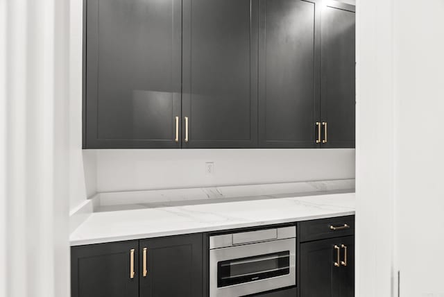 kitchen with light stone countertops, oven, and dark cabinets