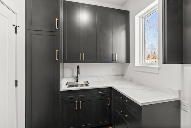 kitchen with a wealth of natural light, light stone countertops, dark cabinetry, and a sink