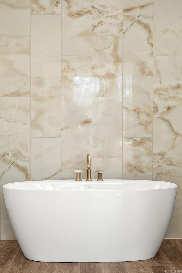 bathroom featuring tile walls, a freestanding tub, and wood finished floors