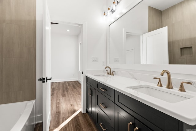 full bath with double vanity, wood finished floors, baseboards, and a sink