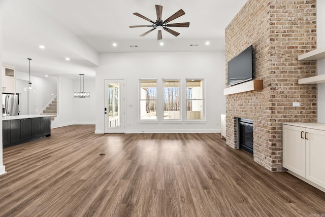 unfurnished living room with stairway, a brick fireplace, recessed lighting, and wood finished floors