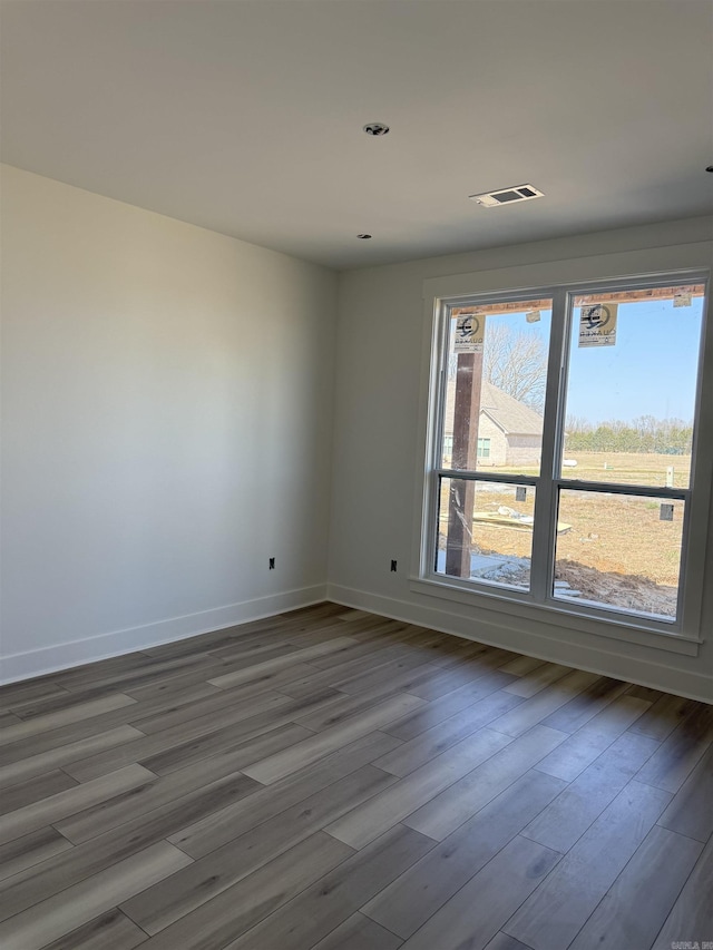 unfurnished room featuring visible vents, baseboards, and wood finished floors