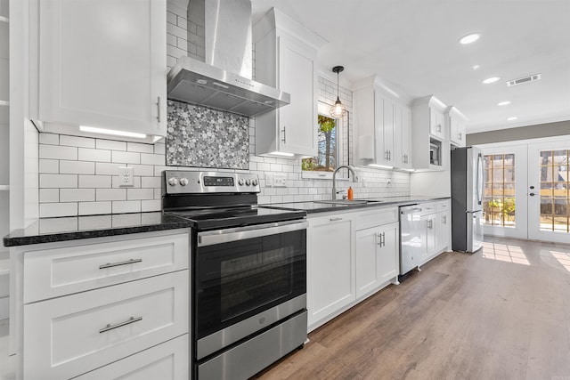 kitchen with light wood finished floors, a sink, french doors, appliances with stainless steel finishes, and wall chimney exhaust hood