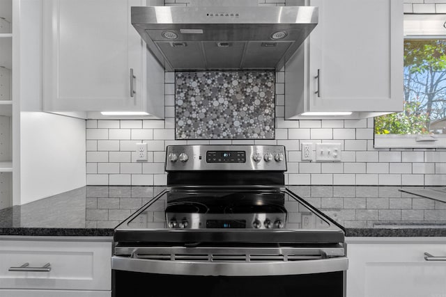 kitchen featuring stainless steel range with electric stovetop, dark stone countertops, backsplash, wall chimney exhaust hood, and white cabinets