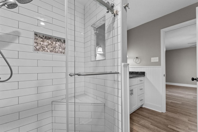 bathroom featuring wood finished floors, vanity, a stall shower, and wainscoting