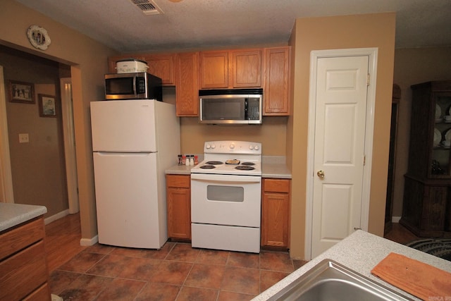 kitchen with visible vents, light countertops, brown cabinets, white appliances, and dark tile patterned flooring