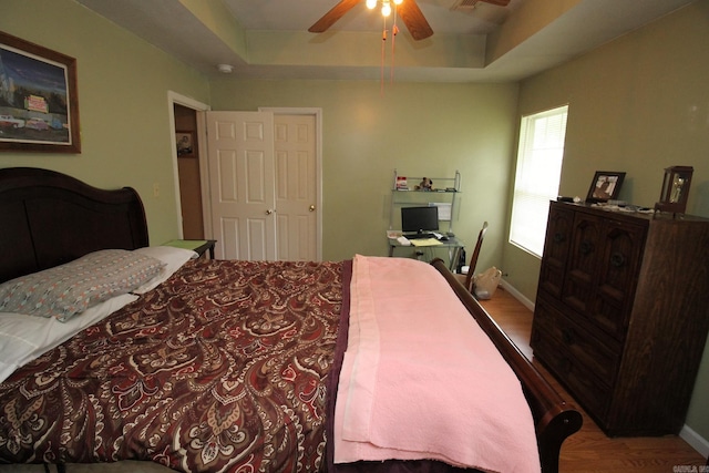 bedroom featuring a tray ceiling, wood finished floors, and baseboards