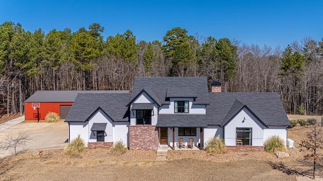 modern farmhouse featuring a wooded view, a chimney, and roof with shingles