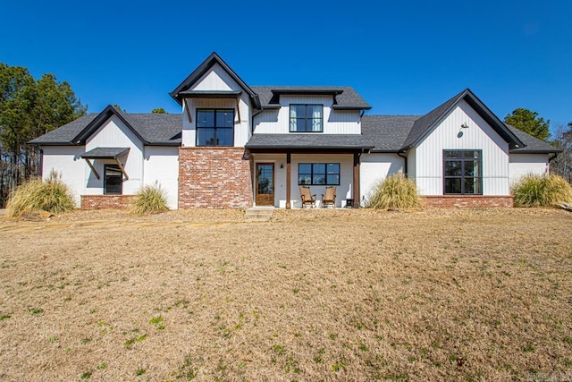 modern farmhouse with brick siding, a front yard, and a shingled roof