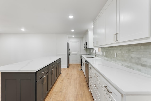 kitchen with light wood finished floors, a center island, decorative backsplash, appliances with stainless steel finishes, and white cabinetry