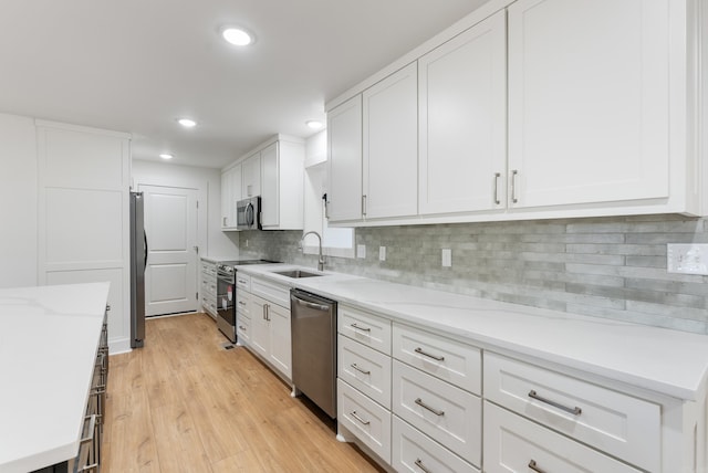 kitchen featuring a sink, stainless steel appliances, light wood-style floors, white cabinets, and decorative backsplash