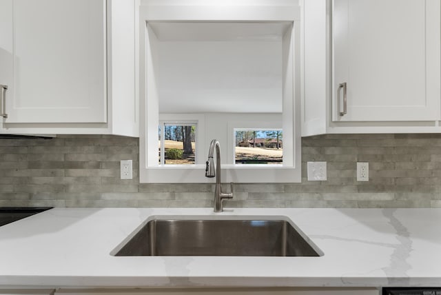 kitchen with white cabinetry, light stone countertops, backsplash, and a sink