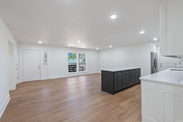 kitchen with light wood finished floors, stainless steel fridge with ice dispenser, light countertops, white cabinets, and a sink