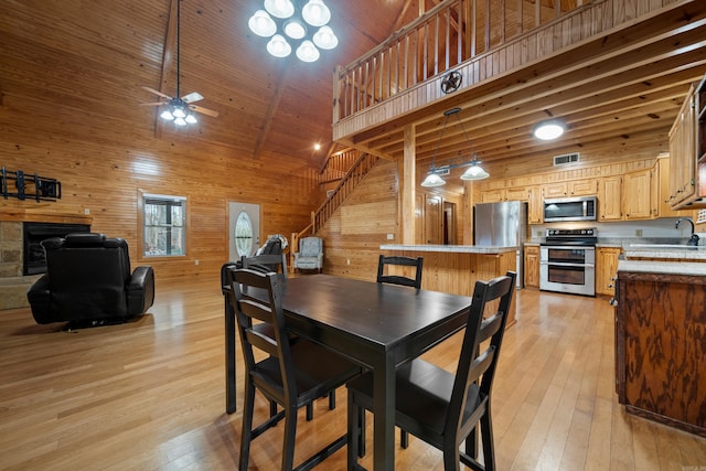 dining area featuring wooden walls, light wood-style flooring, visible vents, and high vaulted ceiling